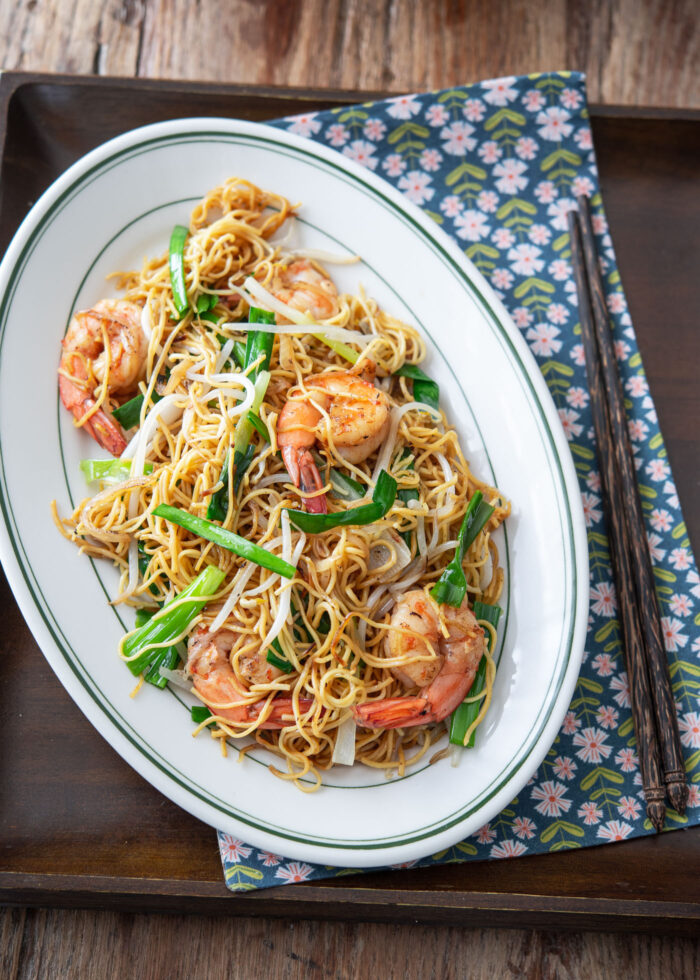 Pan fried noodles with shrimp are served on a platter with chopsticks on a napkin.