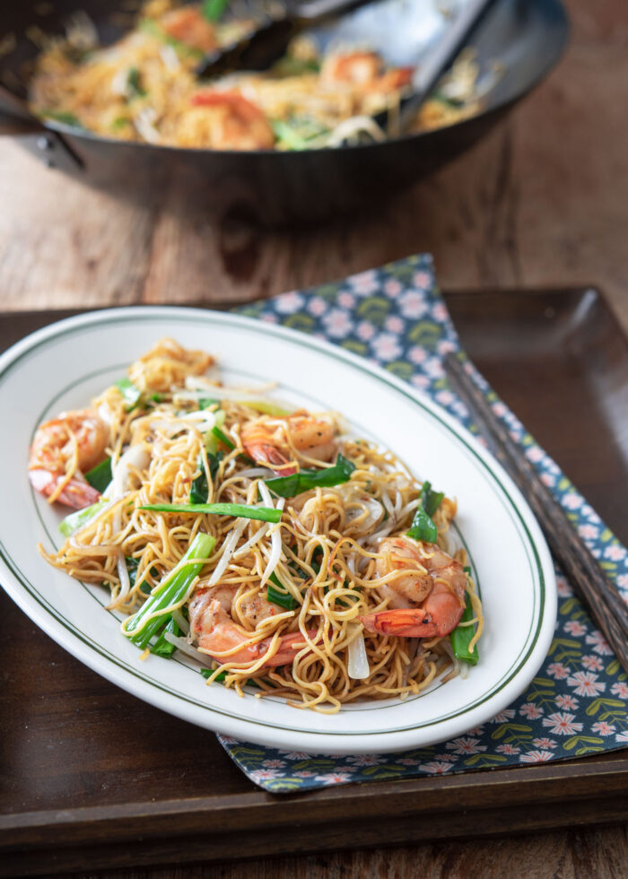 A serving plate is filled with pan fried egg noodles with shrimp and vegetables on a tray lined with a napkin.
