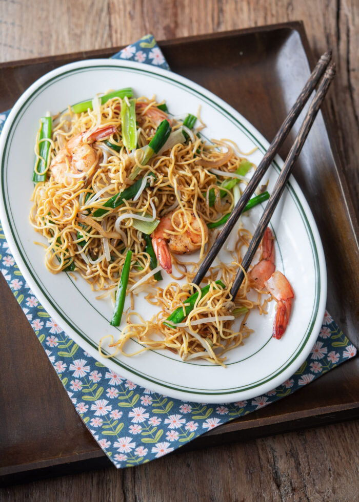 Cantonese pan fried noodles are served on a serving platter with chopsticks on the napkin.