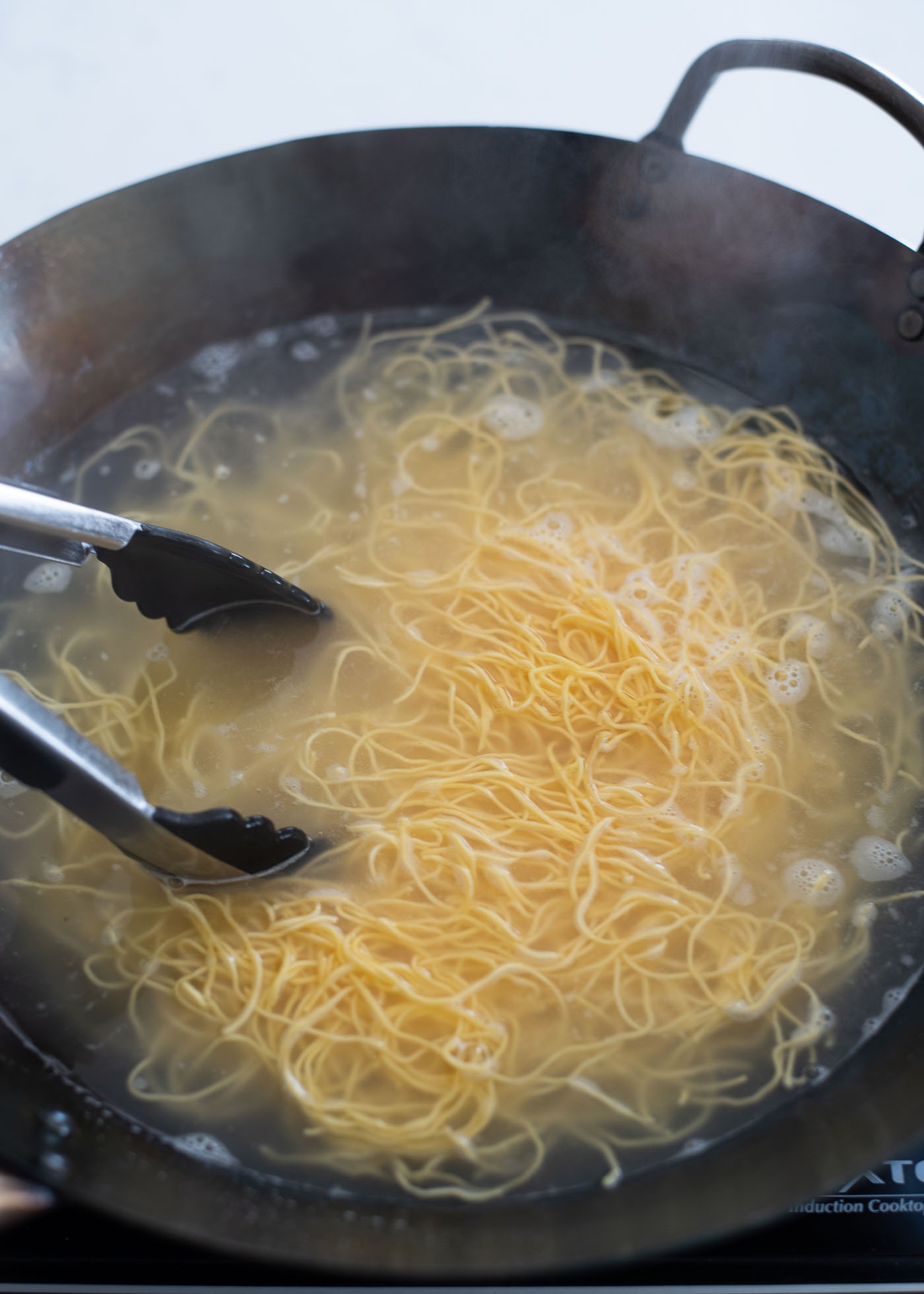 Egg noodles are being cooked in boiling water in a wok.
