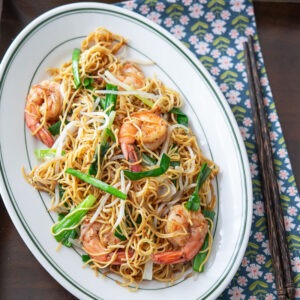 Pan fried noodles with shrimp are served on a platter with chopsticks on a tray lined with a napkin.