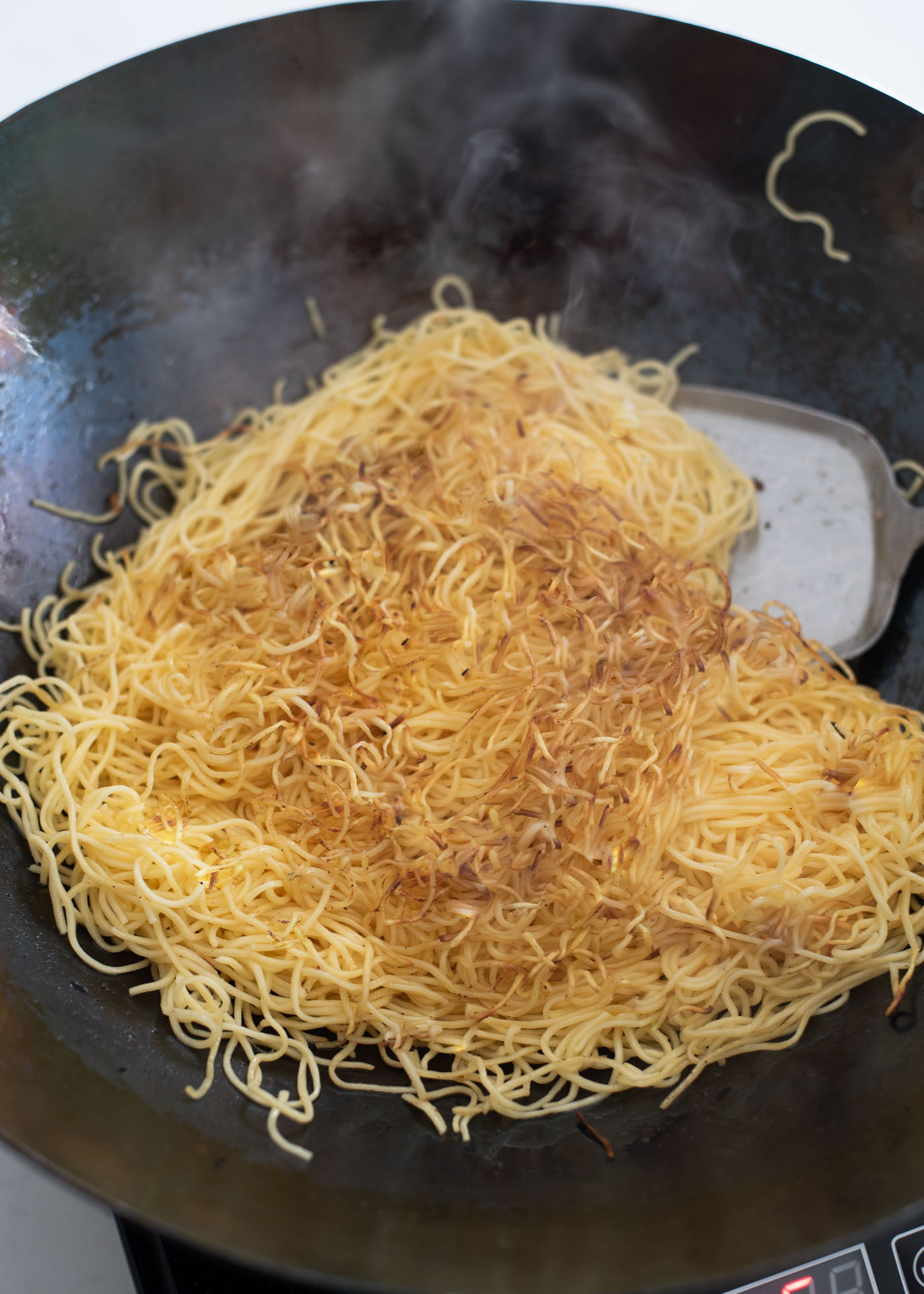 The surface of pan fried egg noodles are showing their golden crispness when flipped to the other side.