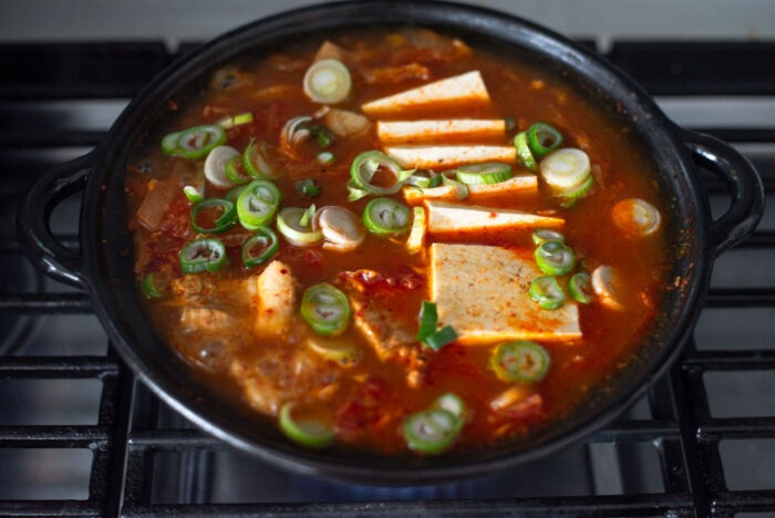 Tofu slices are added to the kimchi jjigae and garnished with chopped green onion.