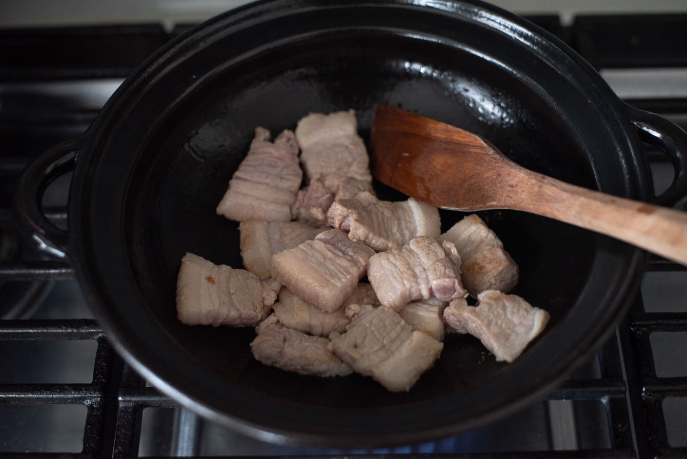 Pork belly slices cooking in a pot to make pork kimchi stew.