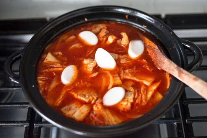 Thin rice cake rounds are added to kimchi stew in a pot.