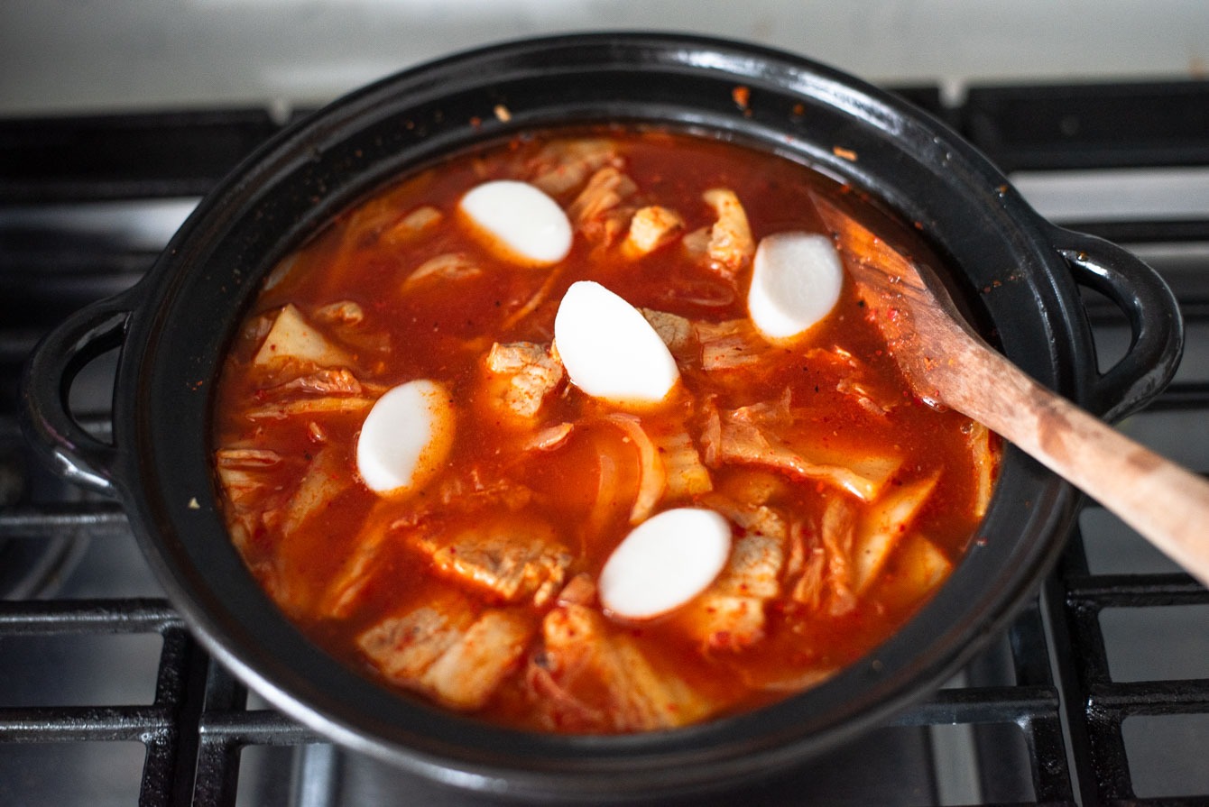 Thin rice cake rounds in a kimchi stew in a pot.