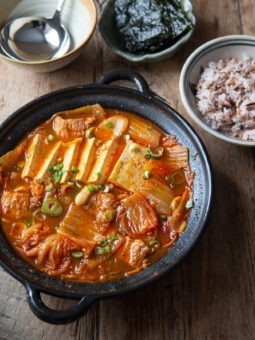 A pot of kimchi jjigae made with pork and tofu is served with rice and roasted seaweed