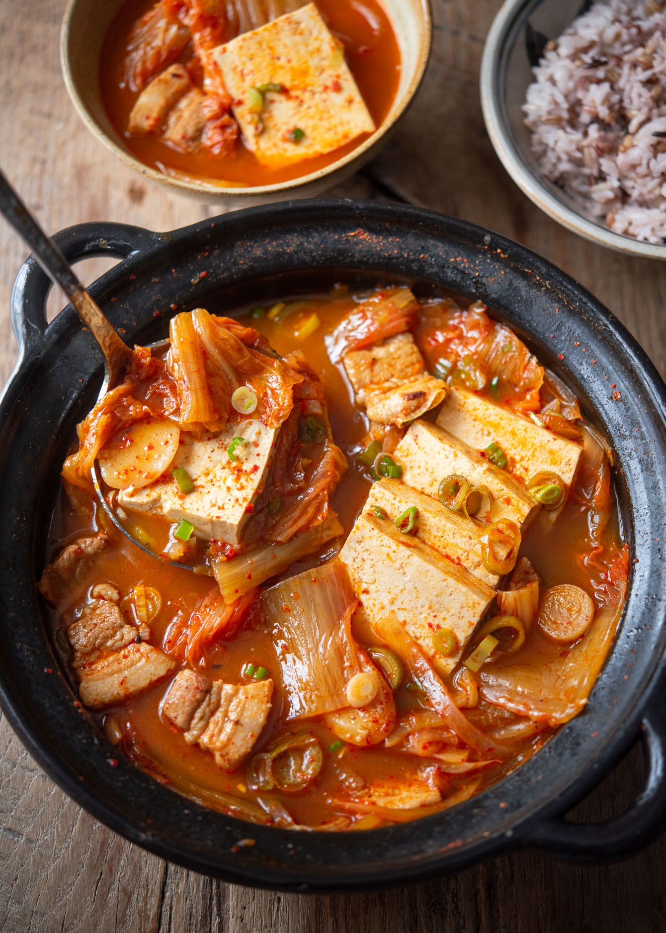 A ladle of kimchi stew (kimchi jjigae) with tofu and pork from the pot.