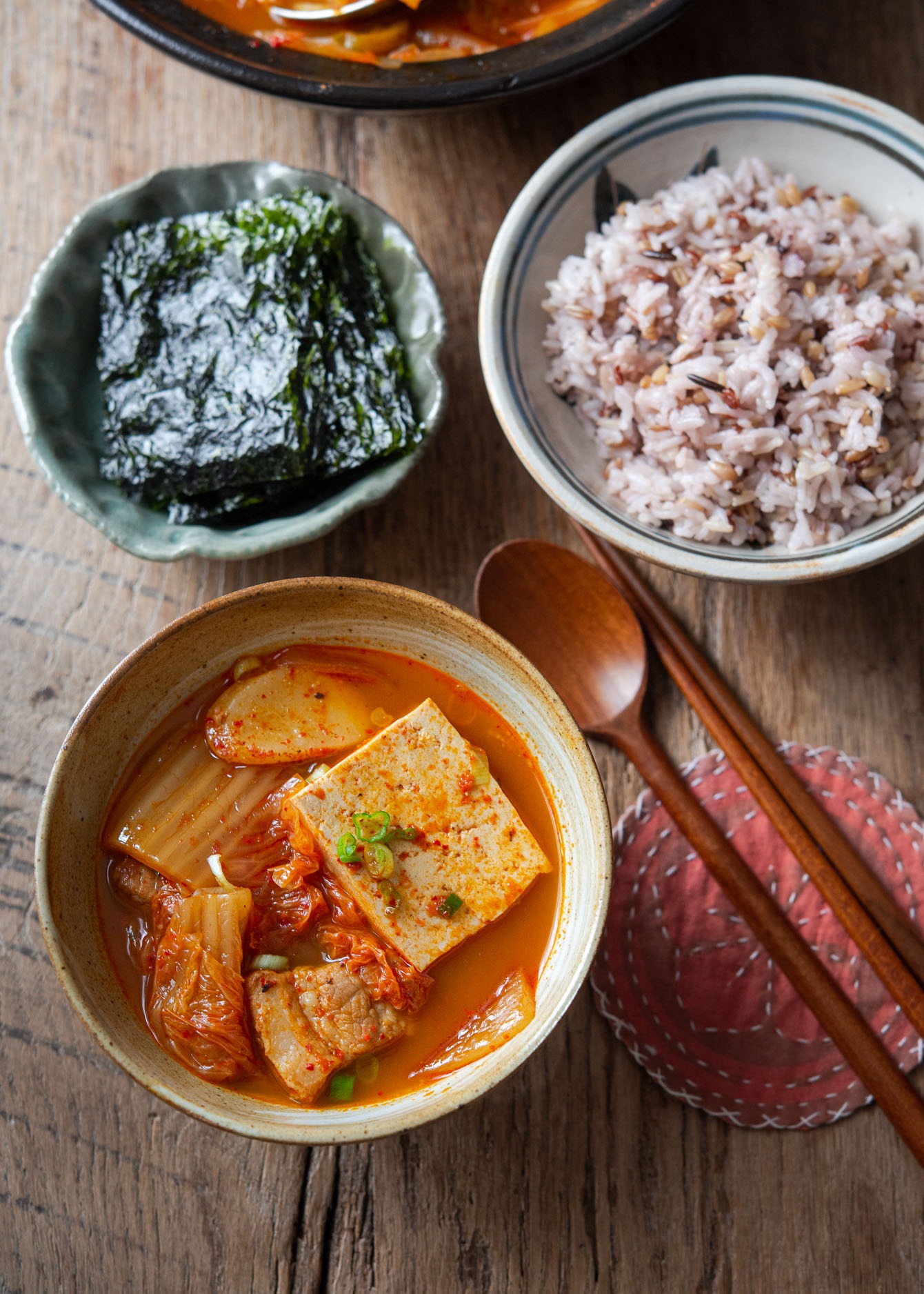 A bowl of pork kimchi jjigae (kimchi stew) with tofu, rice, and roasted seaweed.