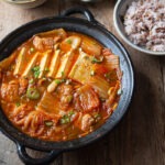 A pot of kimchi jjigae made with pork and tofu is served with rice and roasted seaweed.
