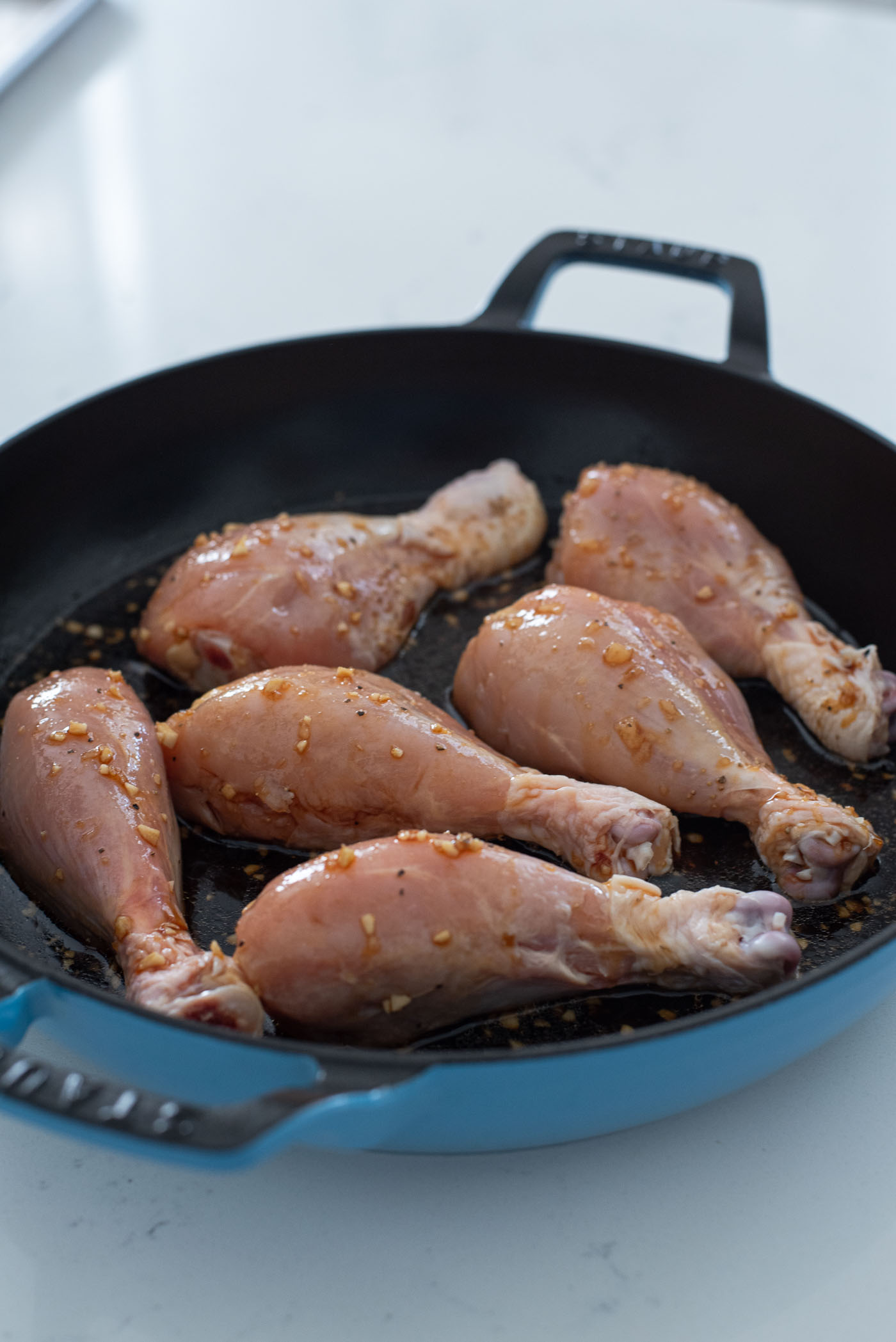 Teriyaki sauce is poured onto chicken drumsticks in the pan.