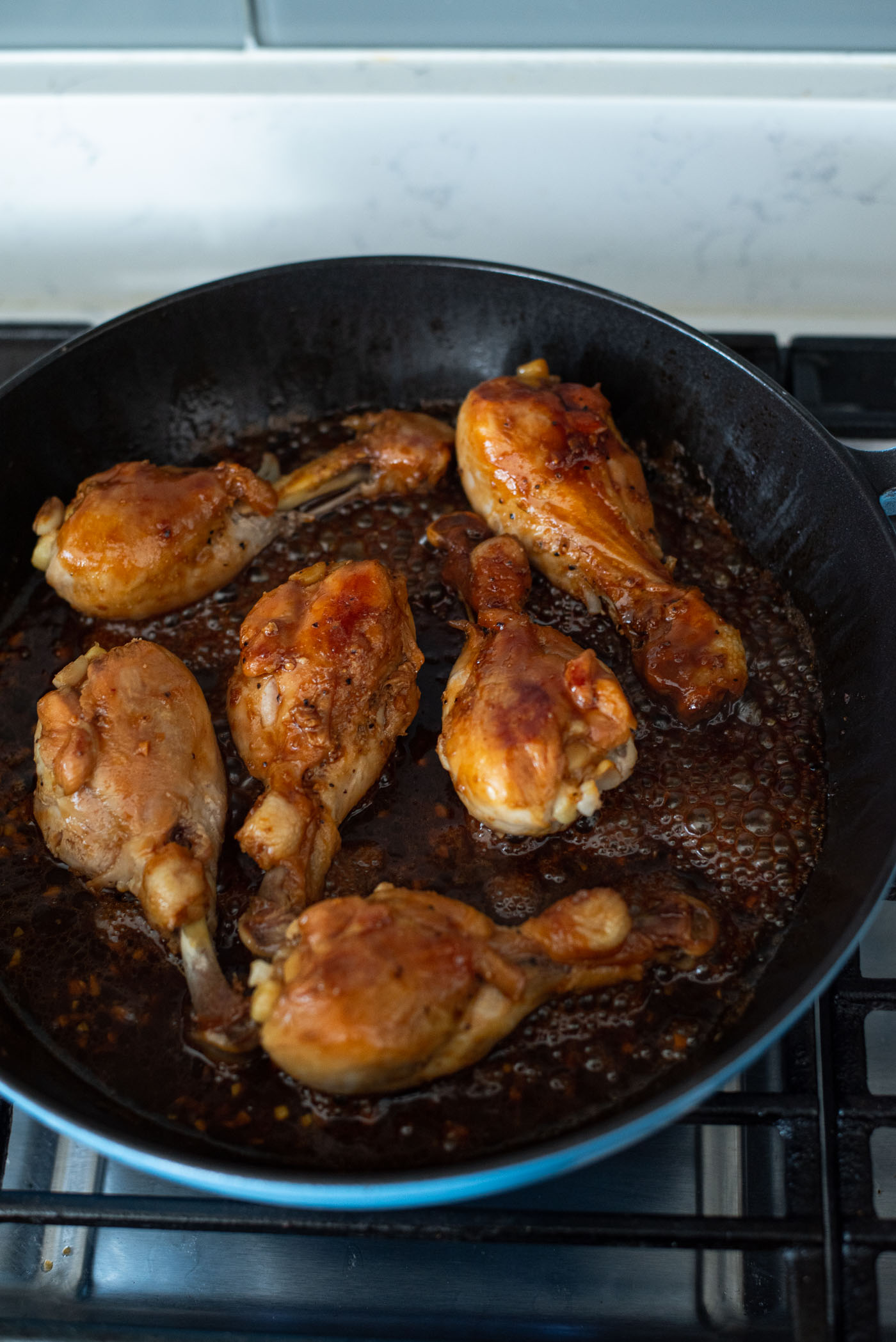 Teriyaki glaze is thickening in the pan coating chicken drumsticks in the pan