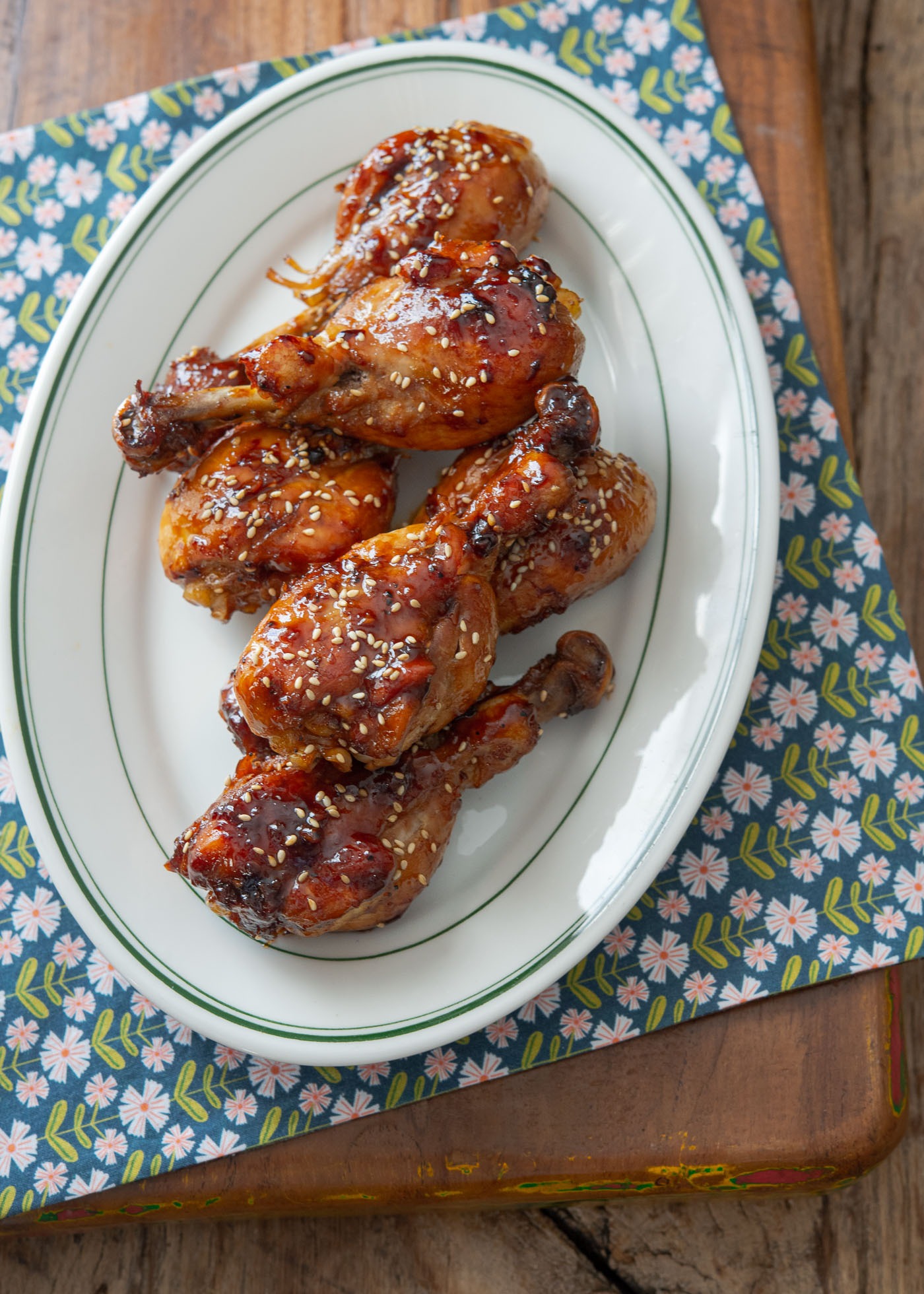 Teriyaki chicken drumsticks are in the oval platter over a floral napkin.