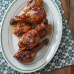 Teriyaki chicken drumsticks are in the oval platter over a floral napkin.