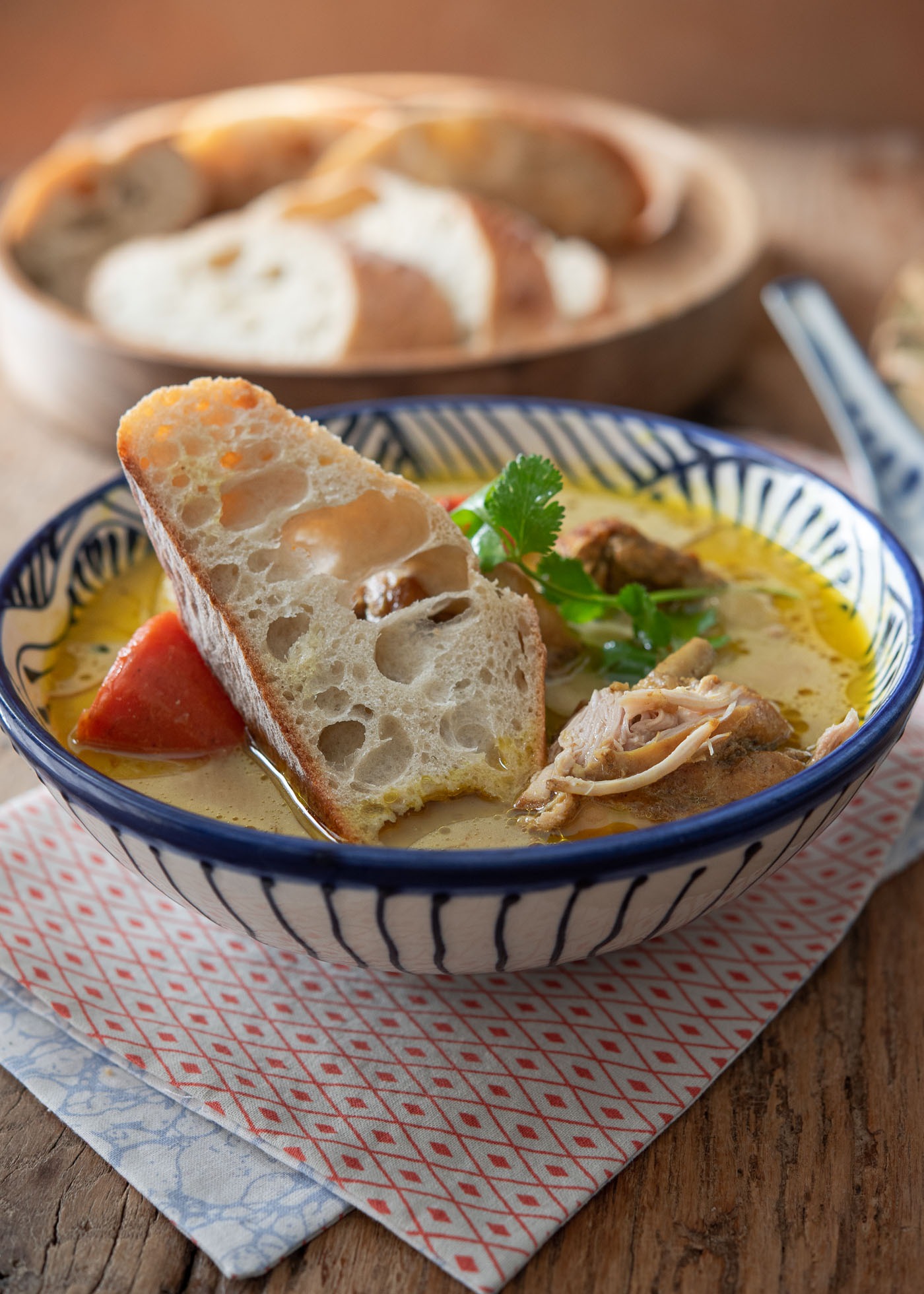 A baguette slice dipped in a bowl of chicken curry soup with potato and carrot