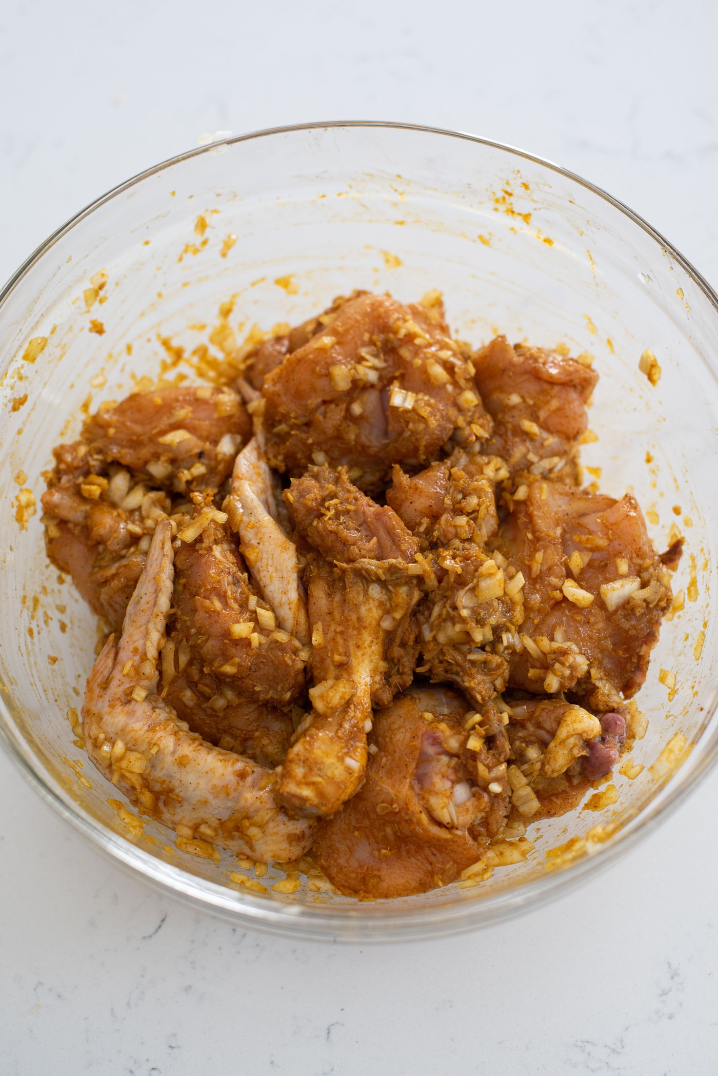 Chicken parts are coated with curry powder and lemongrass paste in a bowl