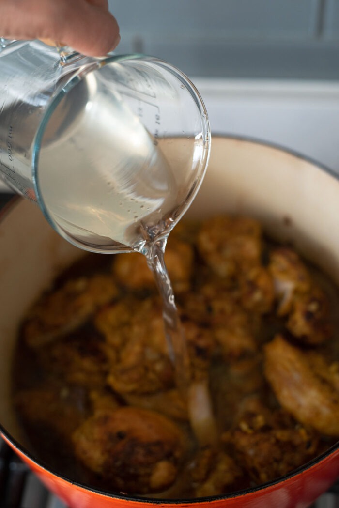 Coconut water is added to browned chicken in a pot.