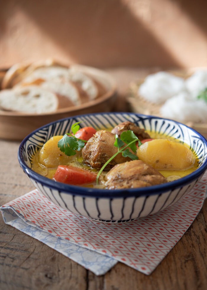 A bowl of Vietnamese chicken curry is garnished with cilantro and served with rice noodles and baguette slices