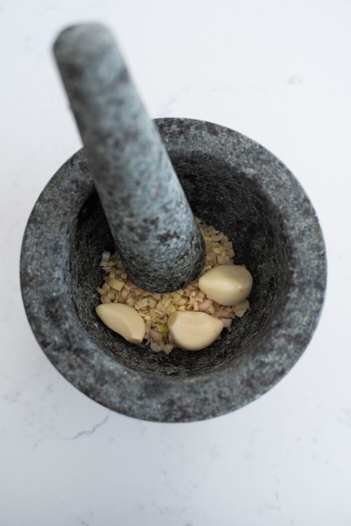 Minced lemongrass and garlic cloves are combined in a mortar with pestle