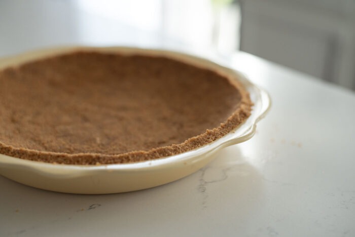 Graham cookie crumbs are pressed into a yellow pie dish