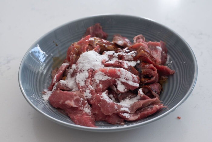 Beef slices are combined with seasoning and potato starch in a bowl