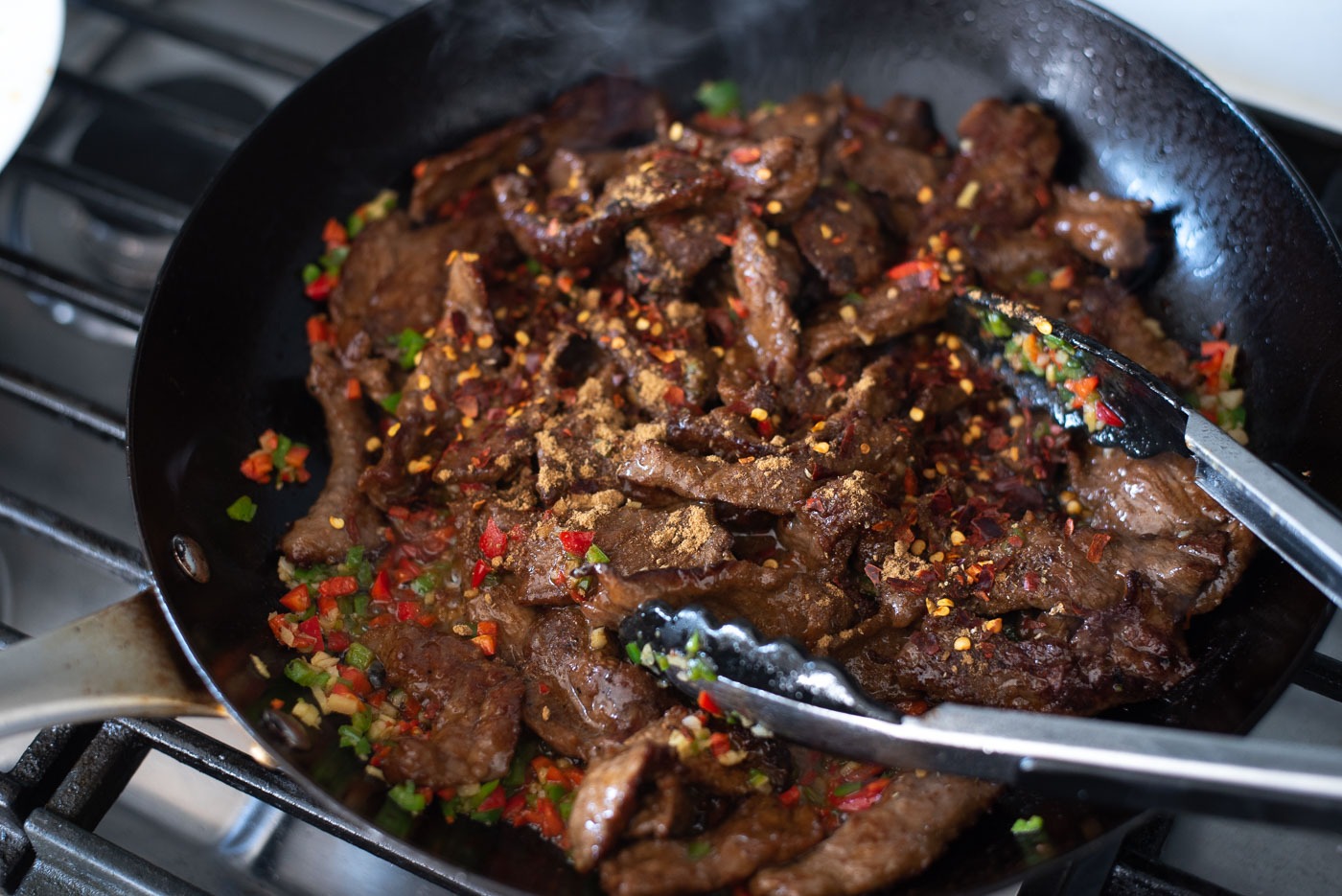 Cumin beef slices are returned to the skillet and mixed with cumin, chili and garlic.