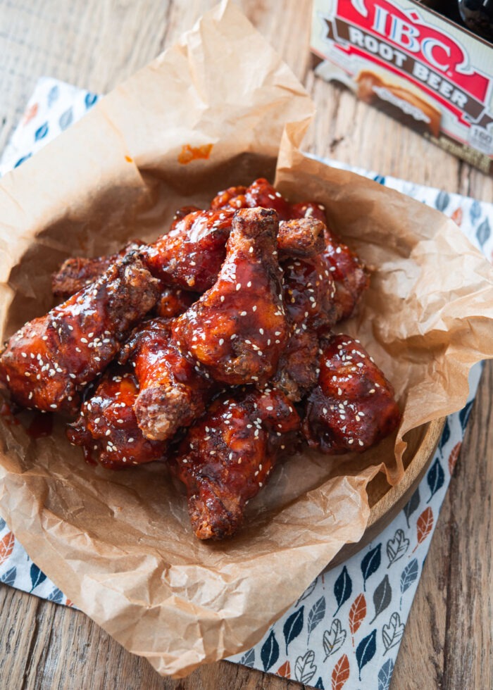 A bunch of fried chicken wings coated with spicy sauce is inside bowl lined with parchment paper