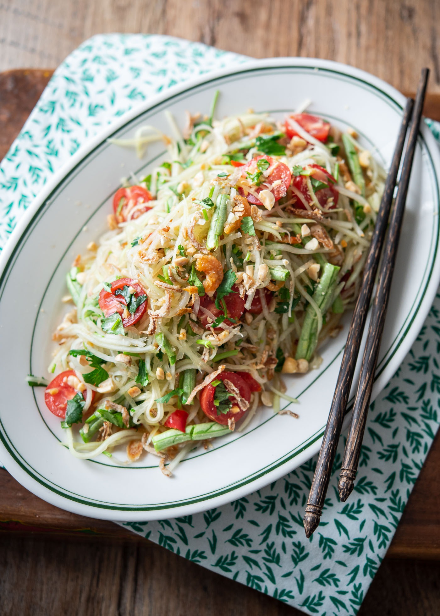 A plate of Thai papaya salad (som tam) garnished with tomato and crushed peanuts.