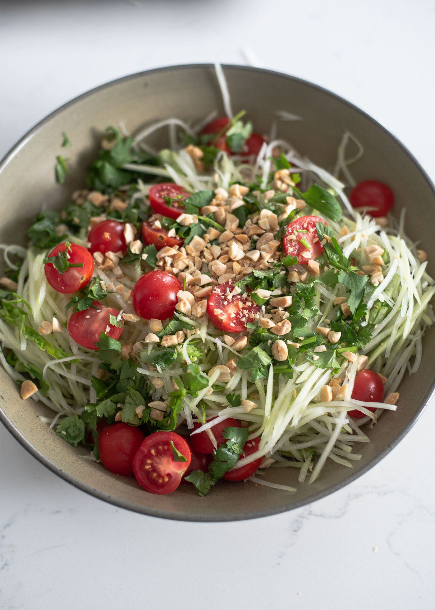 Shredded papaya, tomato, peanuts are combined with salad dressing in a large bowl.