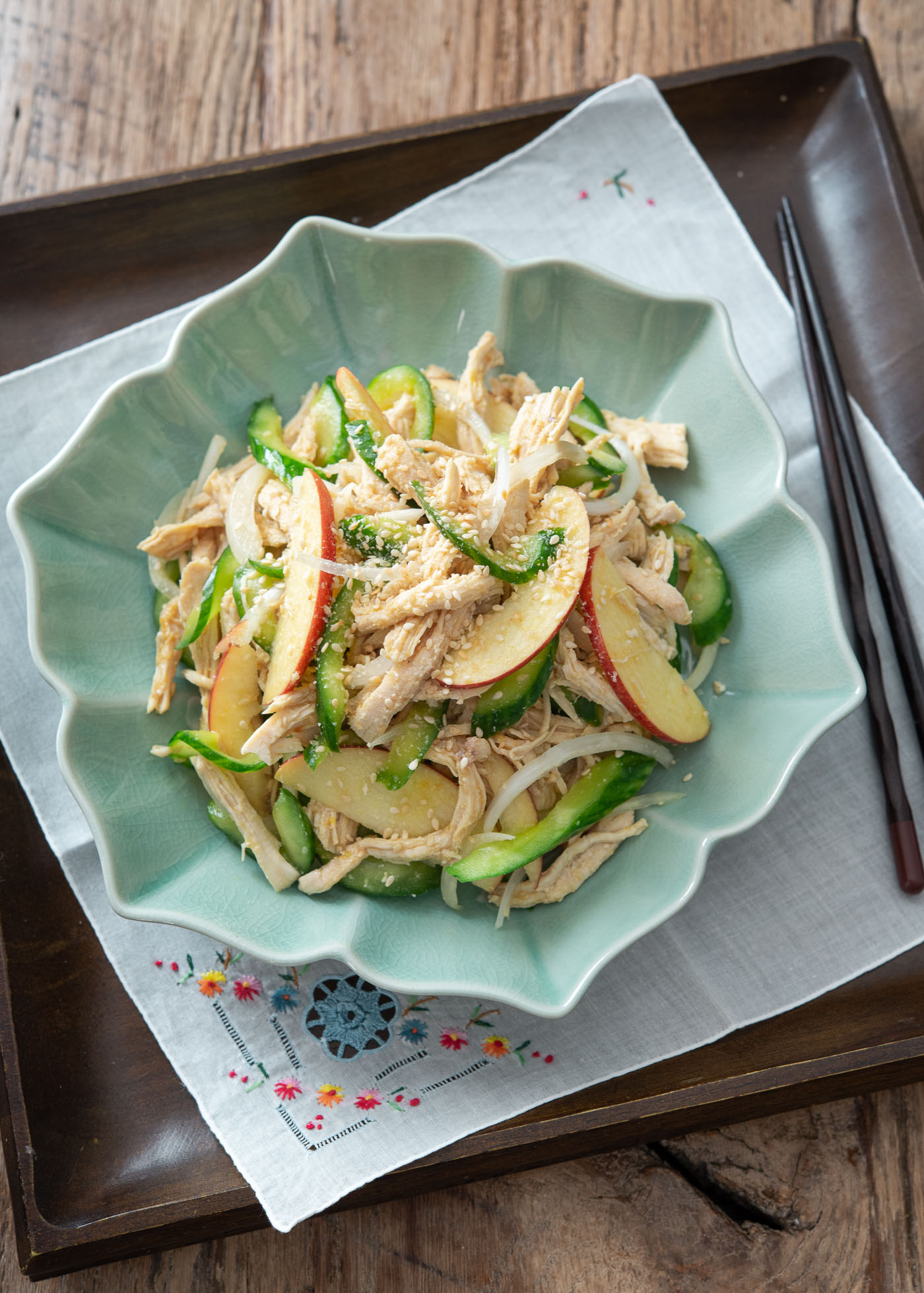 Beautiful Korean chicken salad is served in a teal colored bowl on the tray lined with napkin.