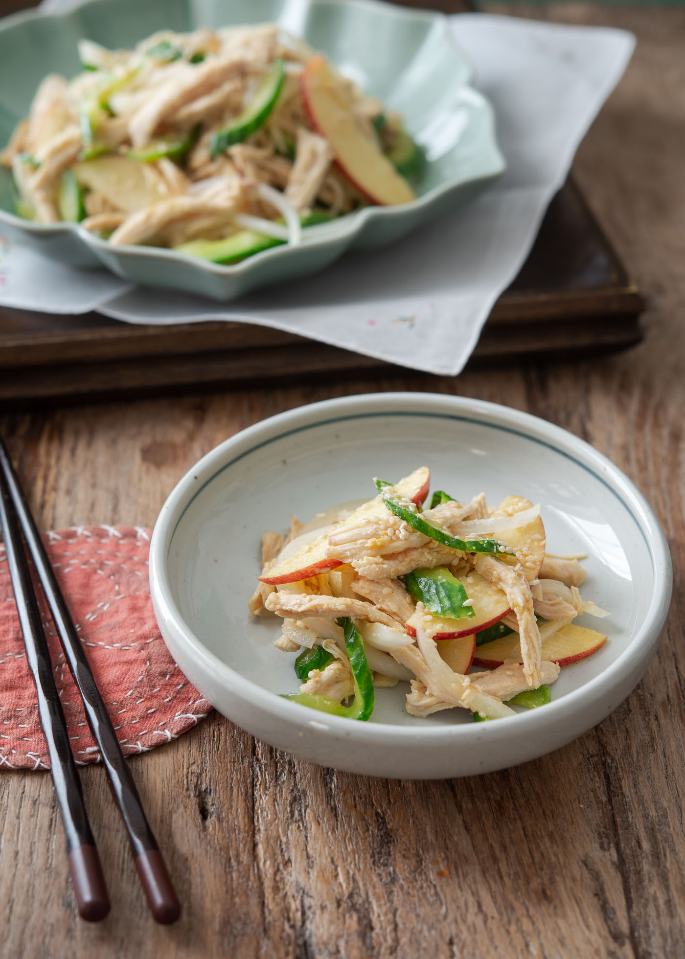 A small portion of Korean chicken salad is placed in a small white serving dish next to chopsticks