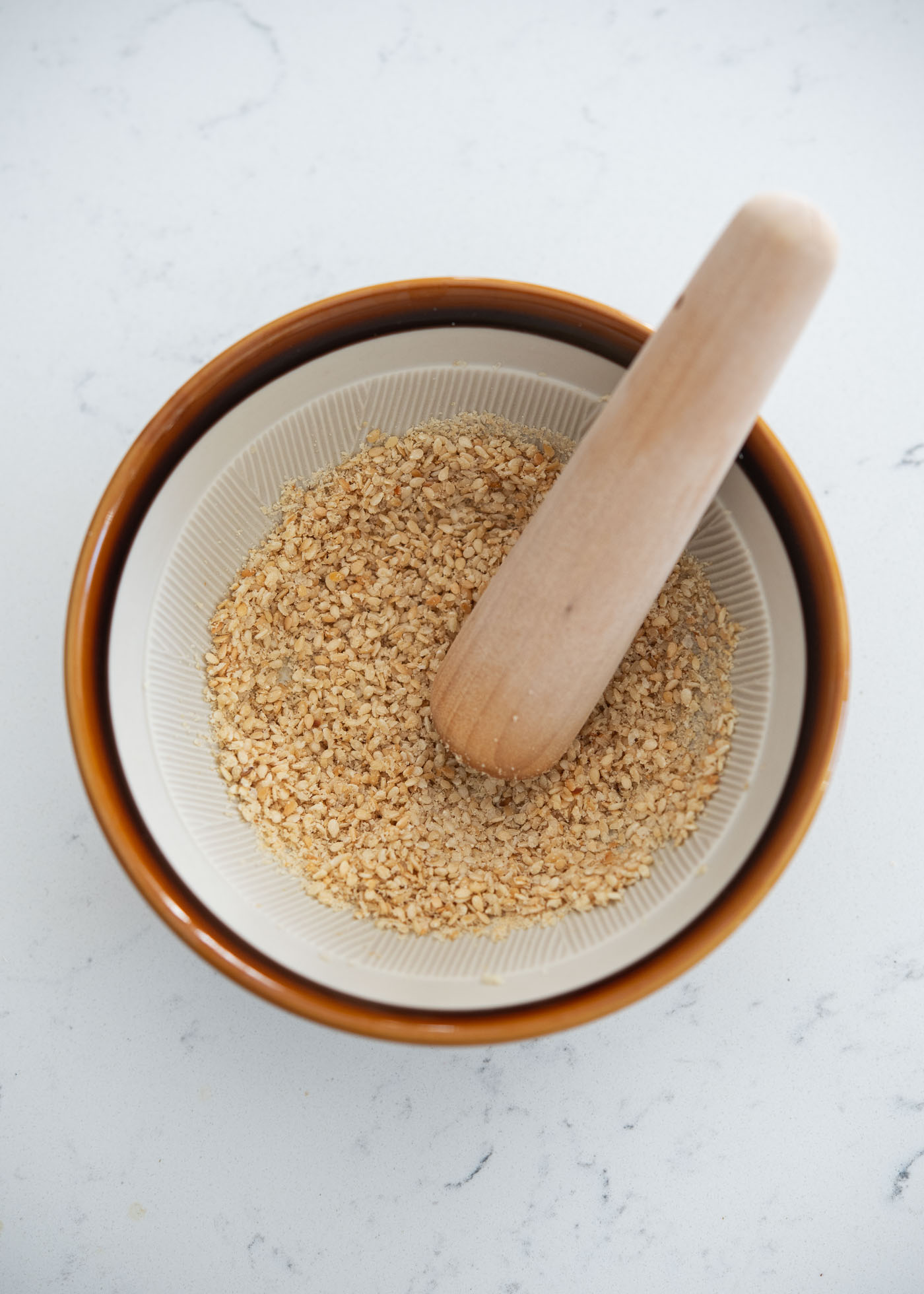 Toasted sesame seeds are being coarsely ground in a small mortar with a pestle.
