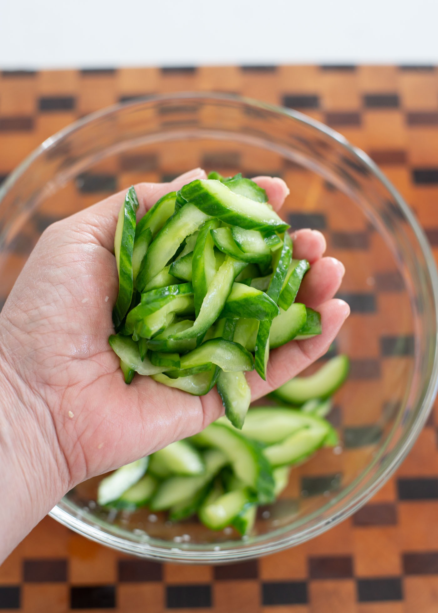 Salted cucumber slices are being squeezed out in hand to remove moisture.