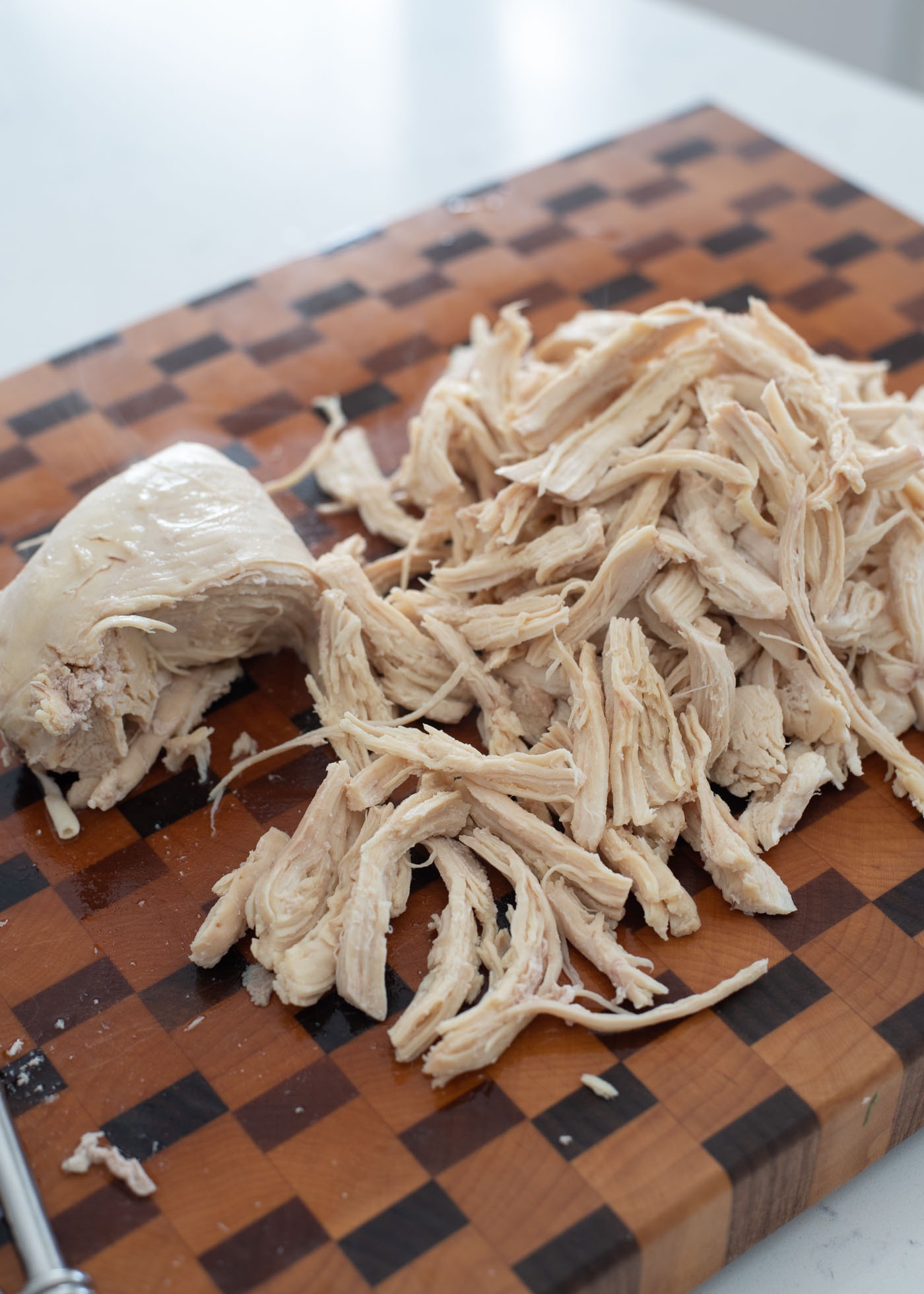 Poached chicken breasts are being shredded on a cutting board.