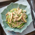 Beautiful Korean chicken salad is served in a teal colored bowl on the tray lined with napkin.