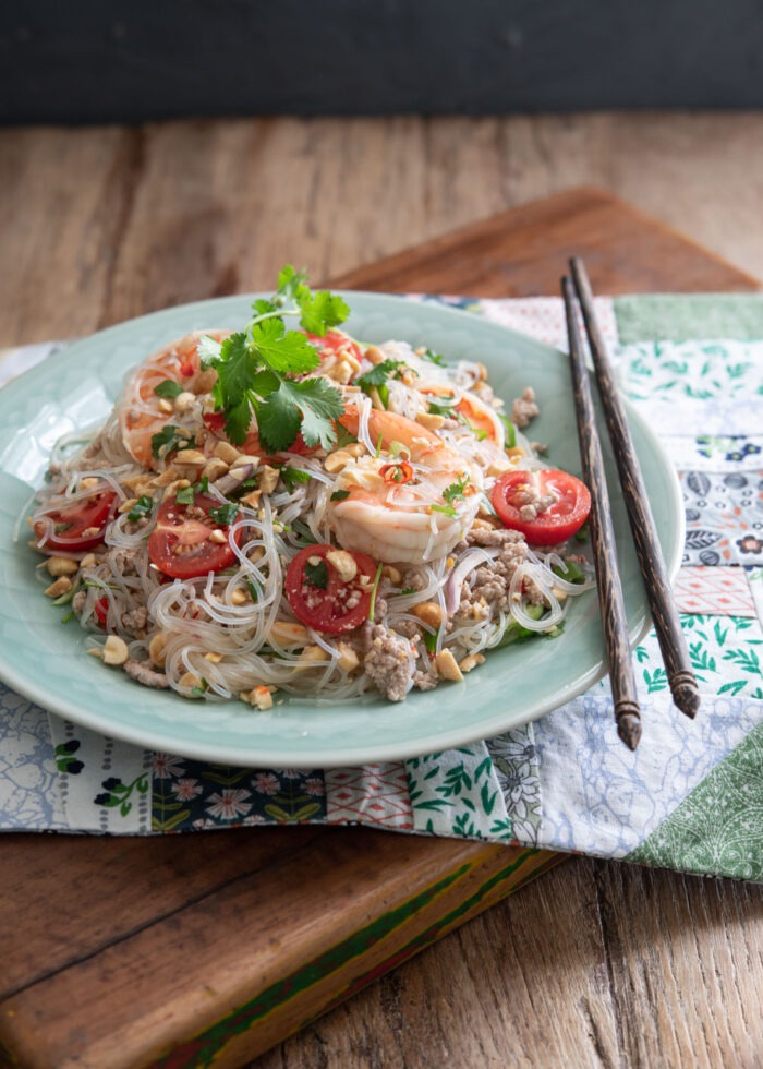 A plate of Thai glass noodle salad is on a placemat with chopsticks