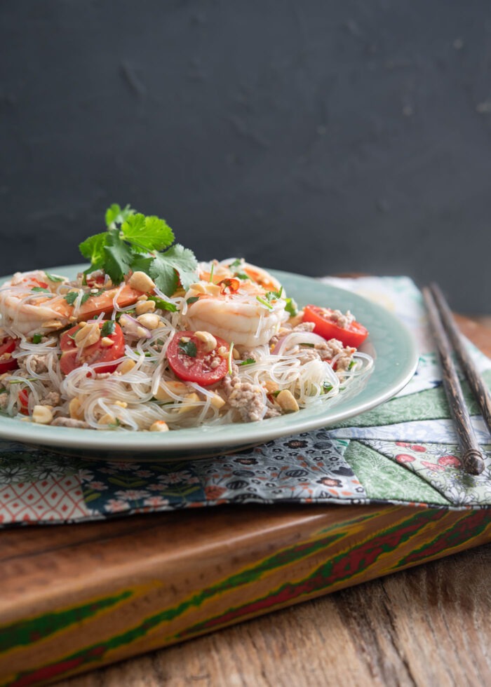 A plate of Thai glass noodles with shrimp is adorned with cilantro and served on a placemat.