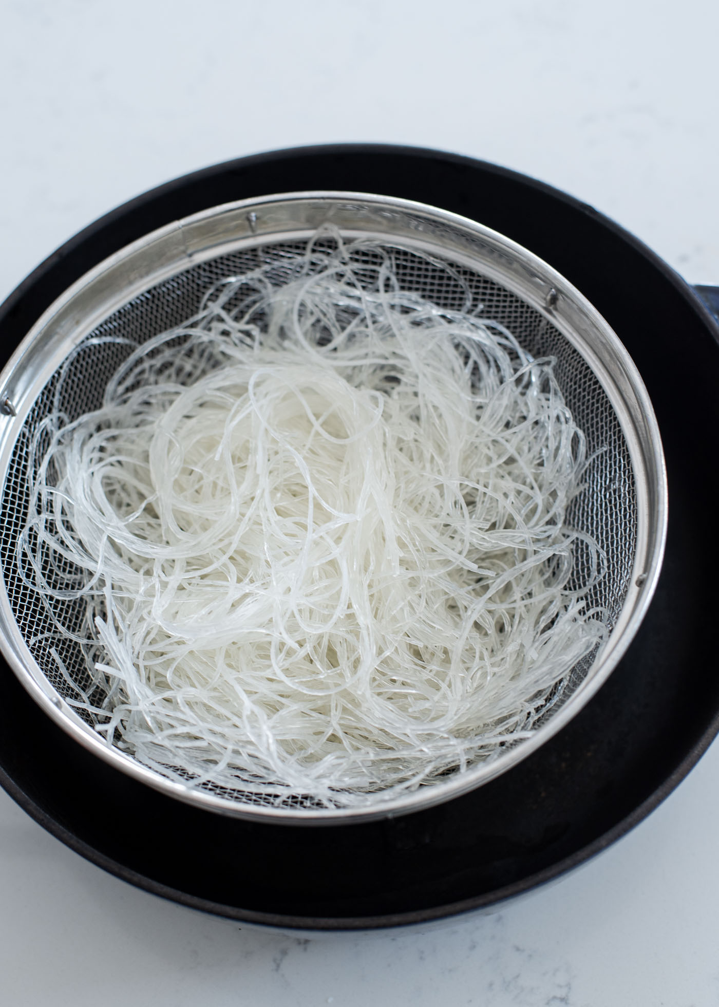 Soaked glass noodles are drained in a colander.