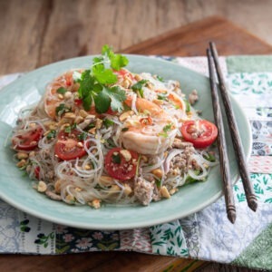 A plate of Thai glass noodle salad is on a placemat with chopsticks