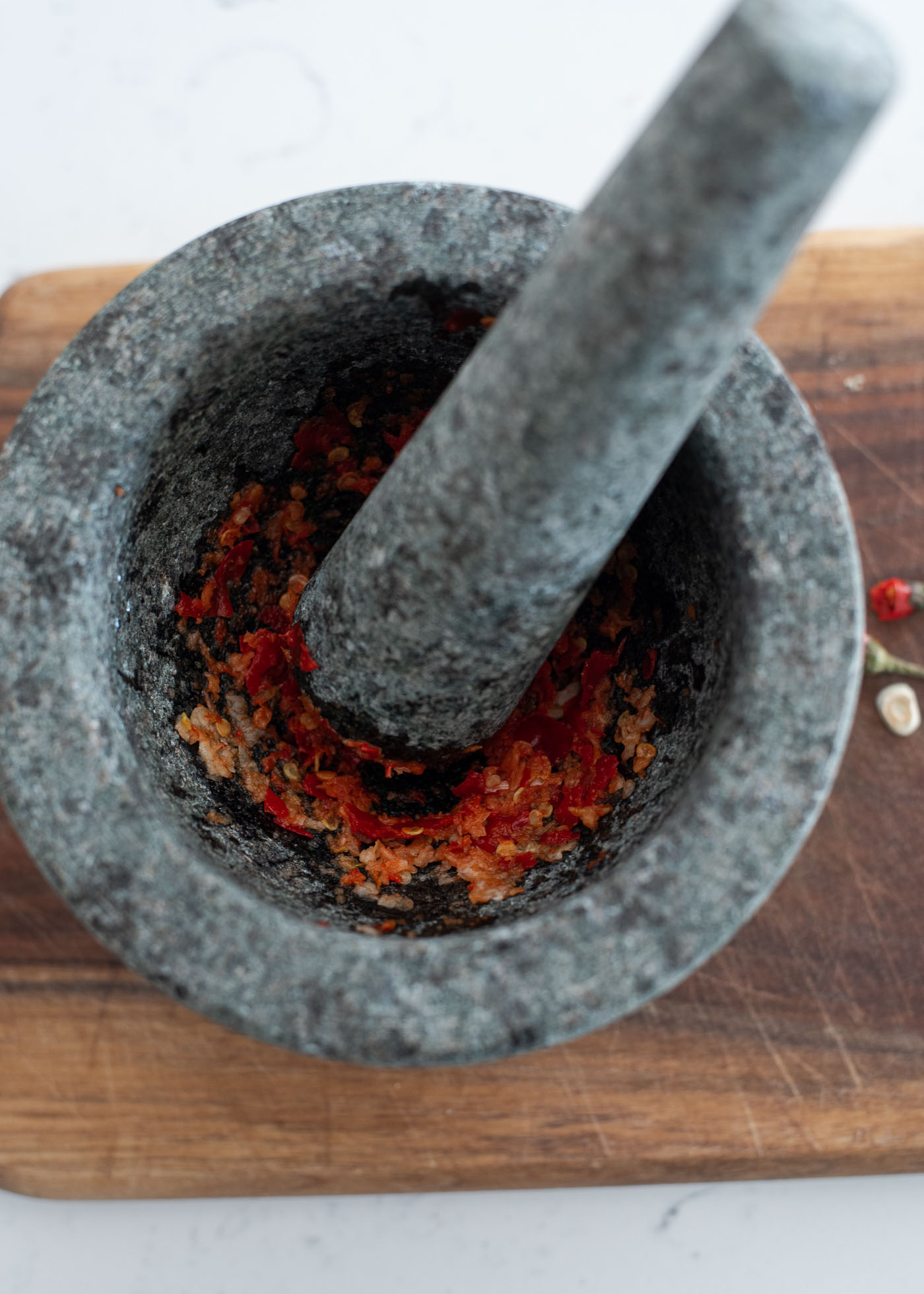 Red chili and garlic is pounded in a mortar with a pestle.