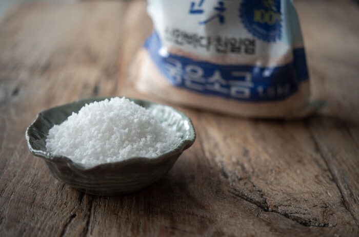 A small bowl is filled with Korean coarse sea salt showing its salt crystals.