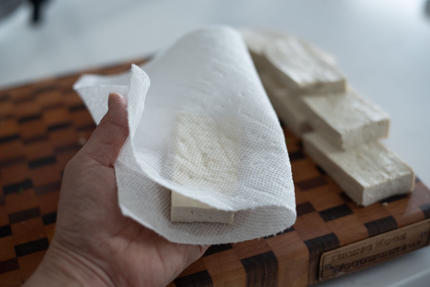 Pressing a slice of tofu with paper towel.