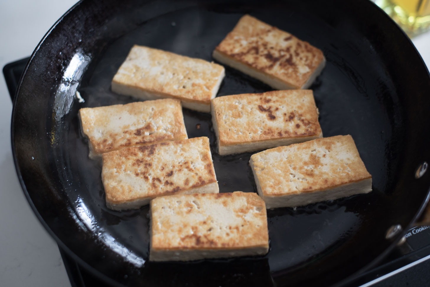 Tofu slices are pan fried in a skillet to golden crisp.