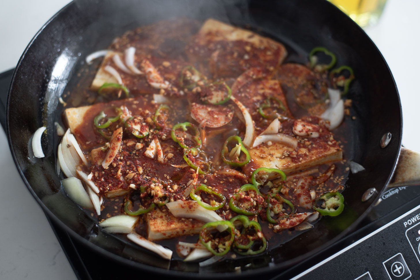 Dubu jorim ssauce and green chili slices are added to tofu slices in a skillet.