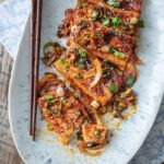 Spicy braised tofu slices are placed in an oval platter with a pair of chopsticks