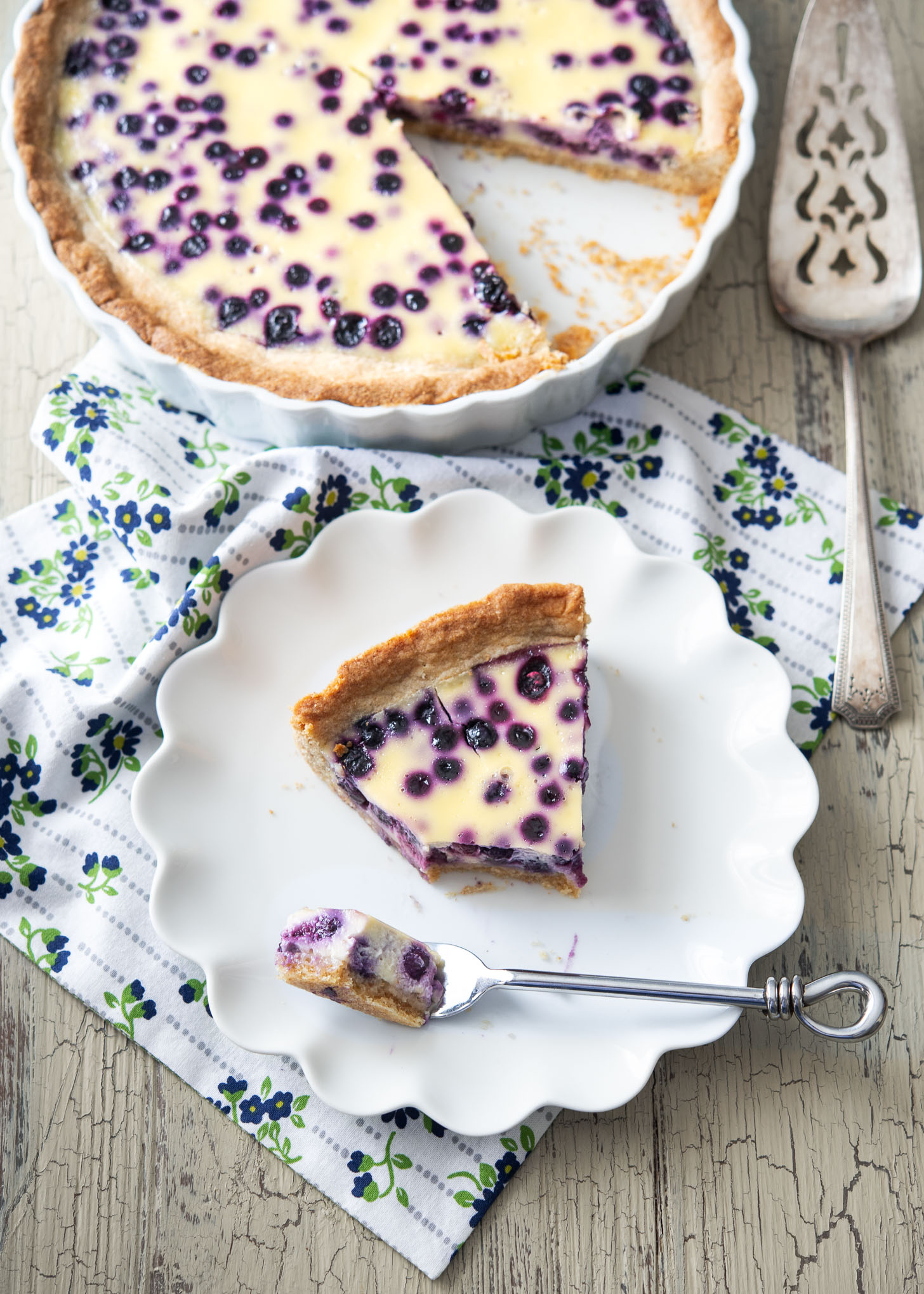 A slice of blueberry pie is served on a white fluted plate.
