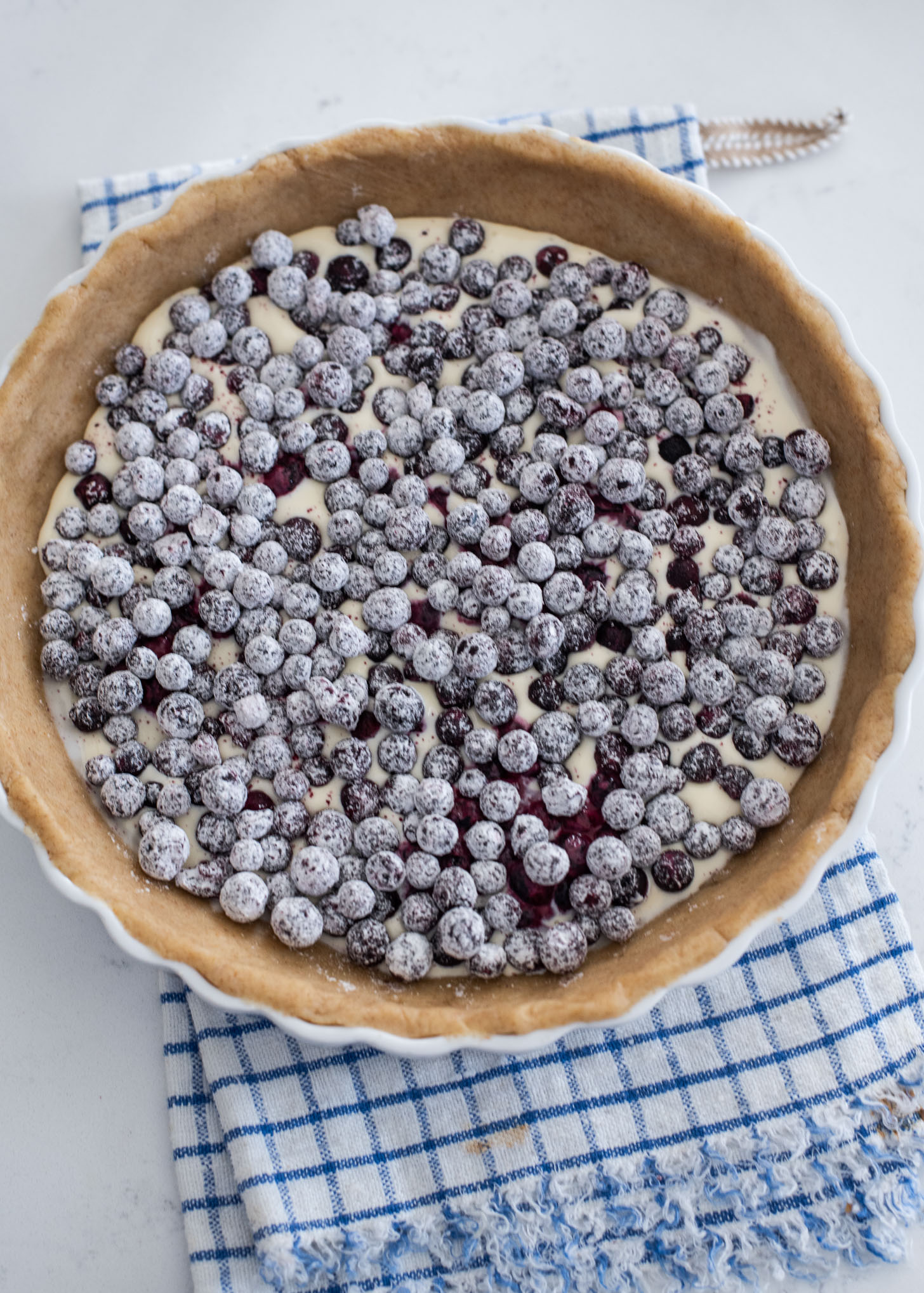 Blueberries coated with flour are placed on a cream filling in a pie crust,