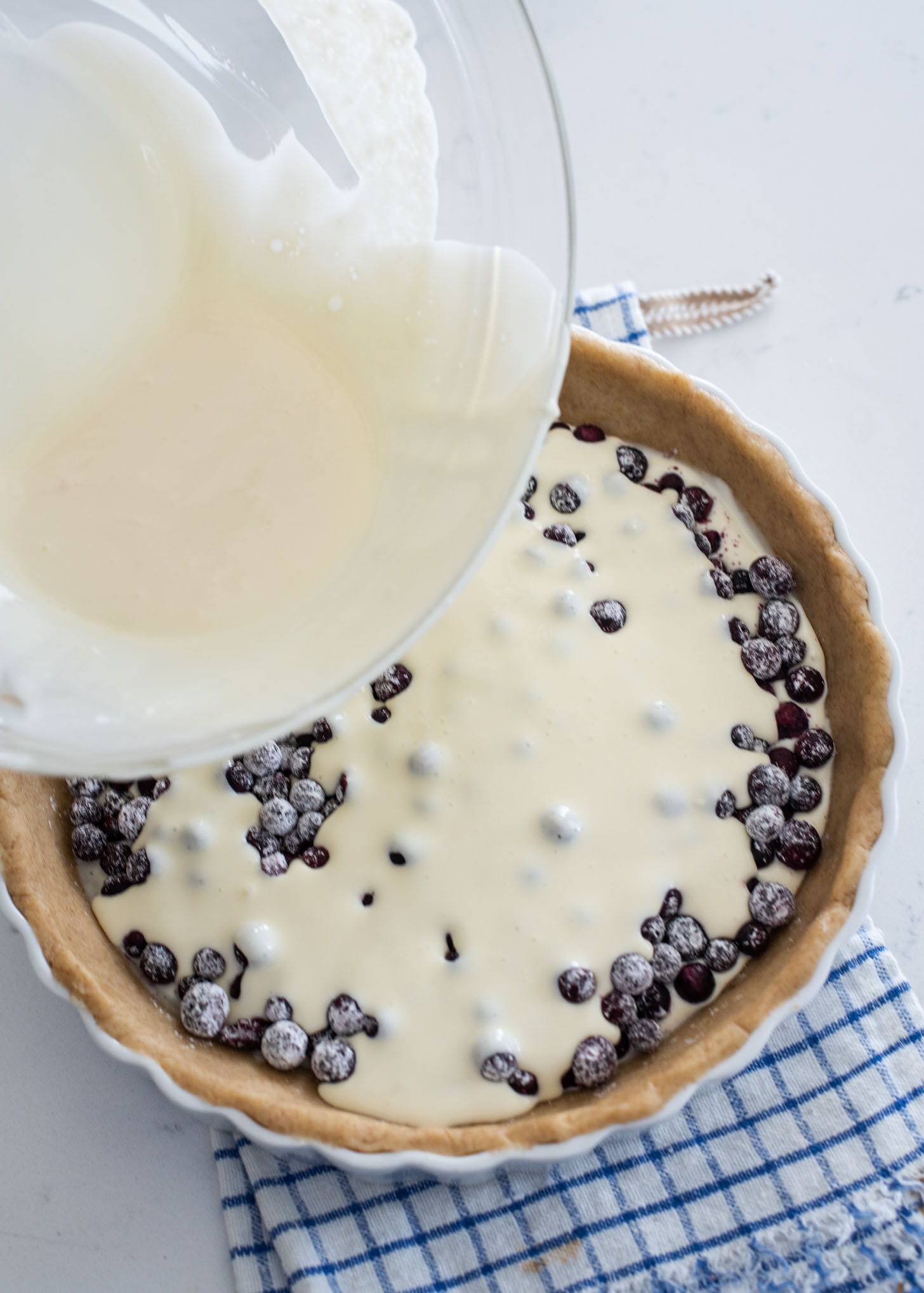 Remaining cream filling being poured over the blueberries in a pie crust.