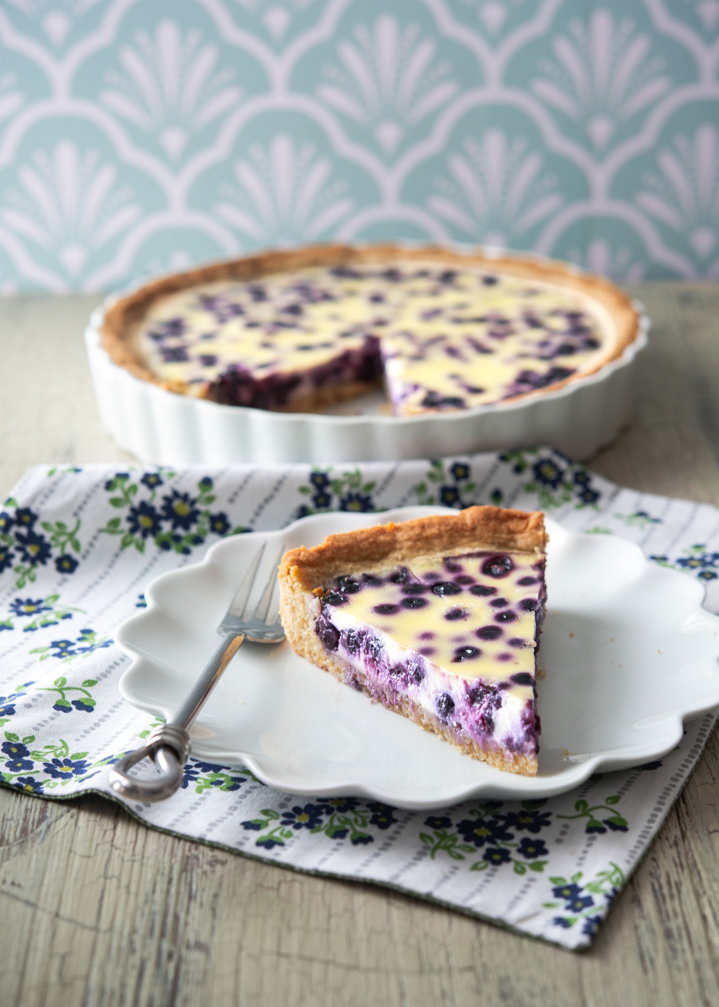 A slice of Finnish blueberry pie (Mustikkapiirakka) served on a white fluted plate.