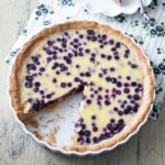 A piece of Finnish blueberry pie is sliced off from a pie dish and served on a small plate.